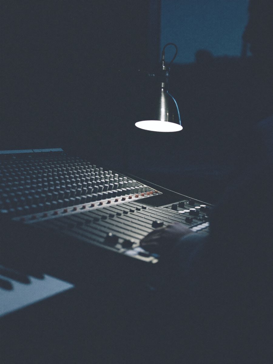 Hands resting on a mixing console in a studio lit by a single lamp.